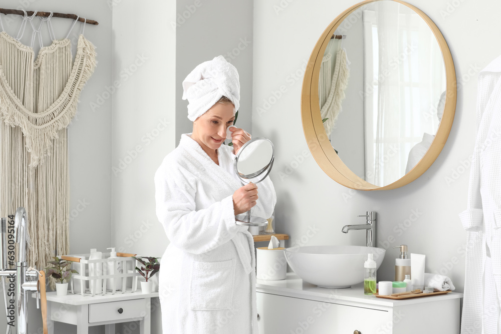 Mature woman applying cosmetic product with cotton pad in bathroom