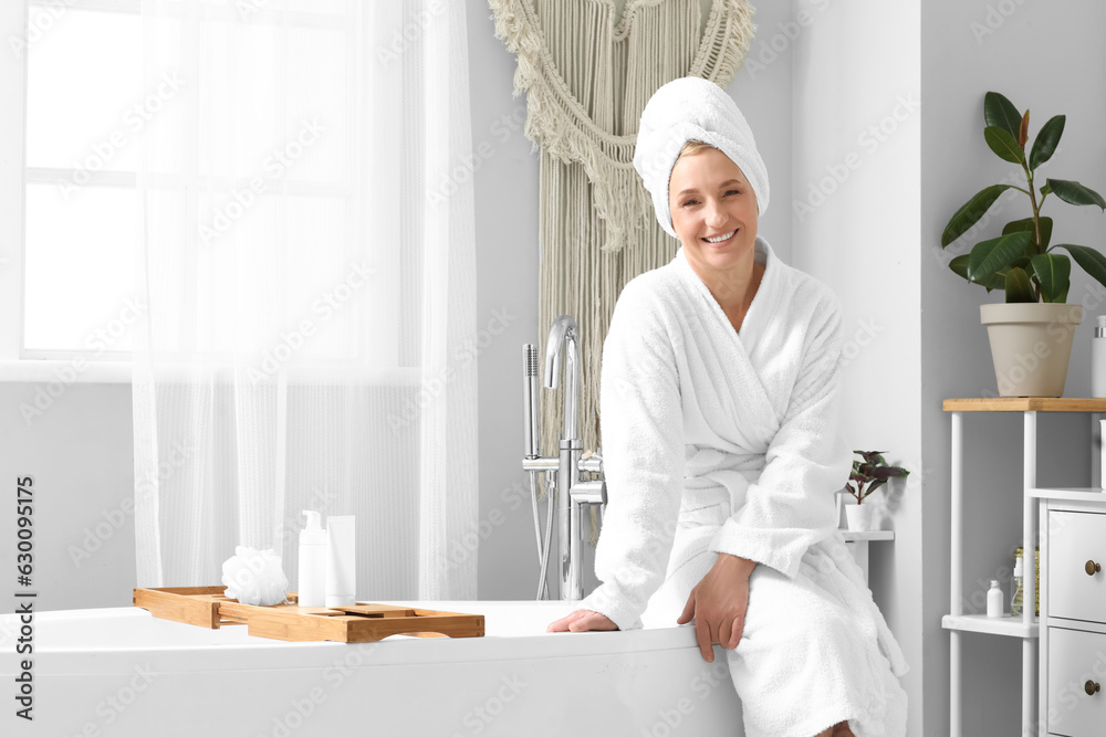 Mature woman with towel sitting in bathroom