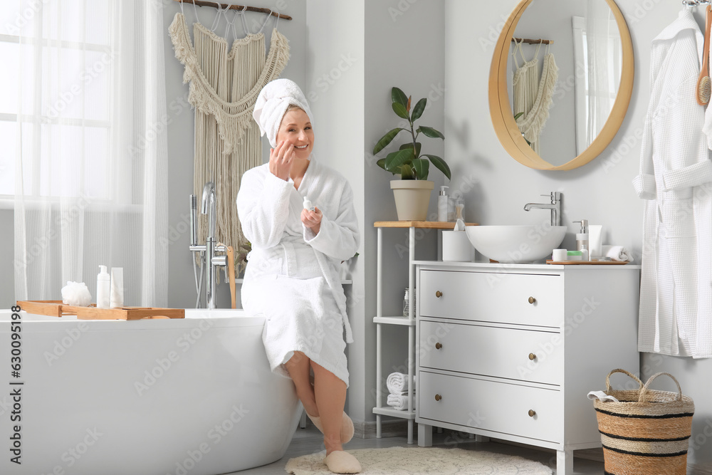 Mature woman applying essential oil in bathroom