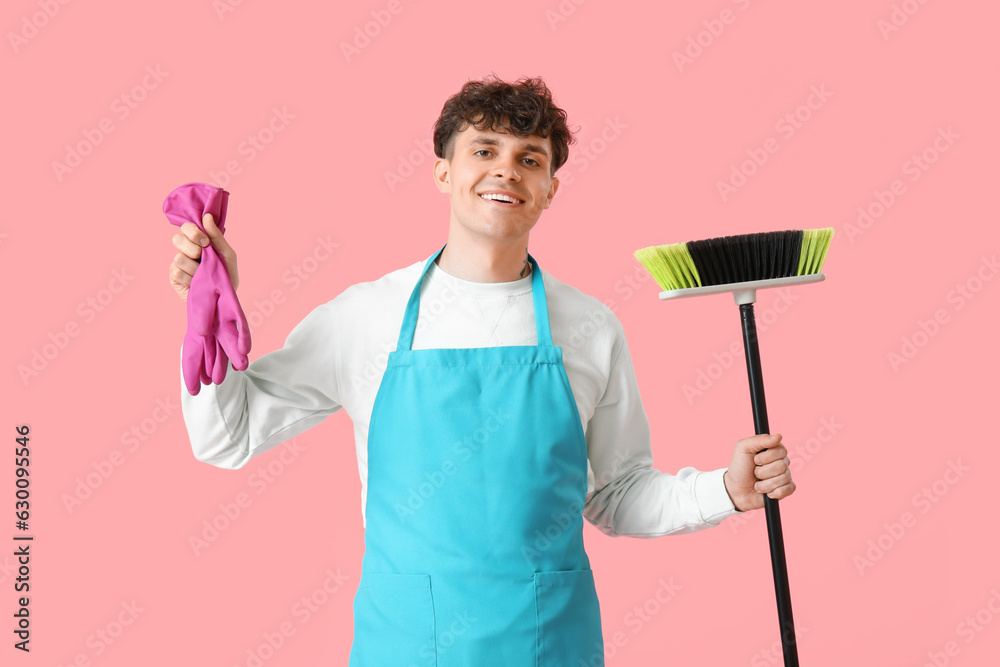 Male janitor with broom and rubber gloves on pink background