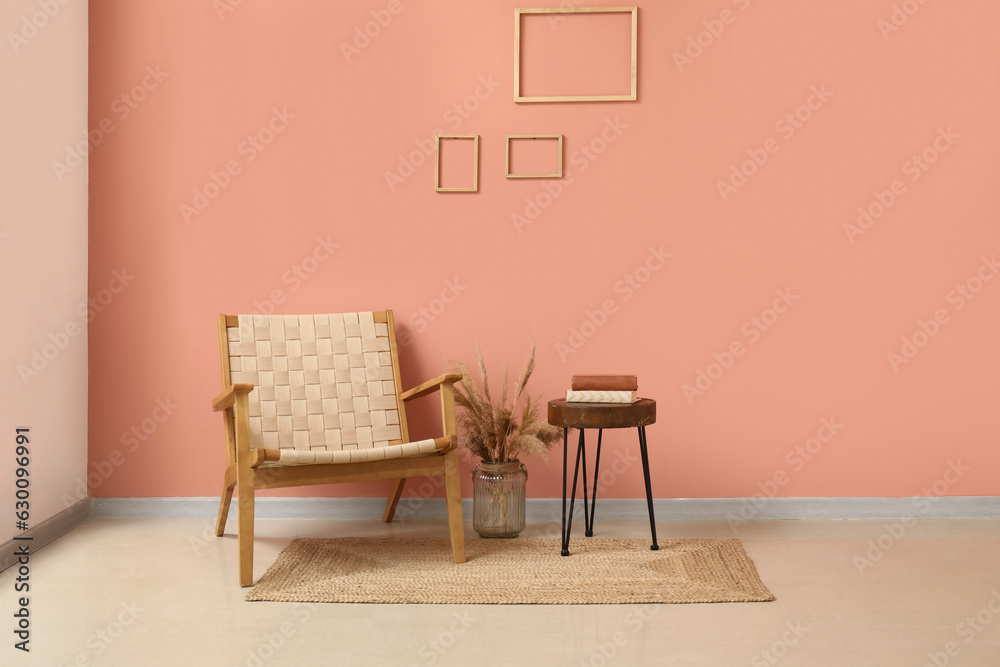 Cozy armchair, vase with pampas grass and books on stool near pink wall