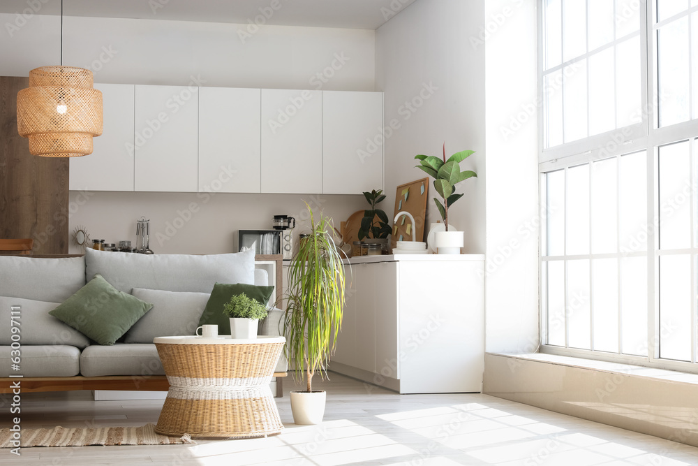 Interior of light living room with cozy grey sofa, coffee table and glowing lamps near big window