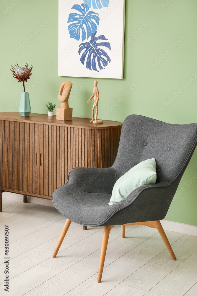 Dark grey armchair with pillow, dresser and sculptures near green wall