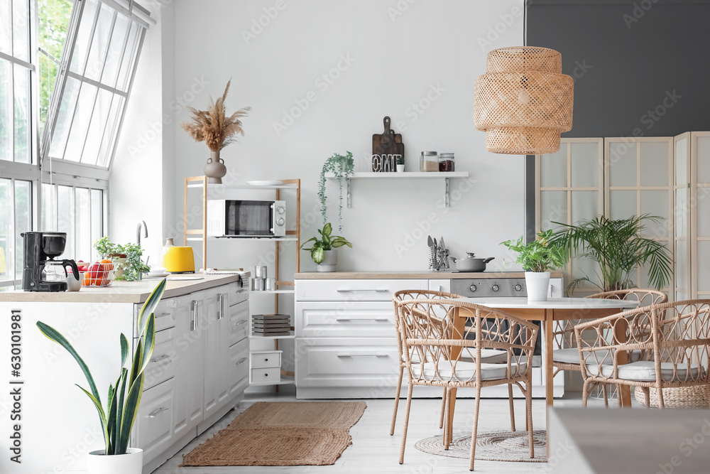 Interior of light kitchen with white counters, dining table and big window