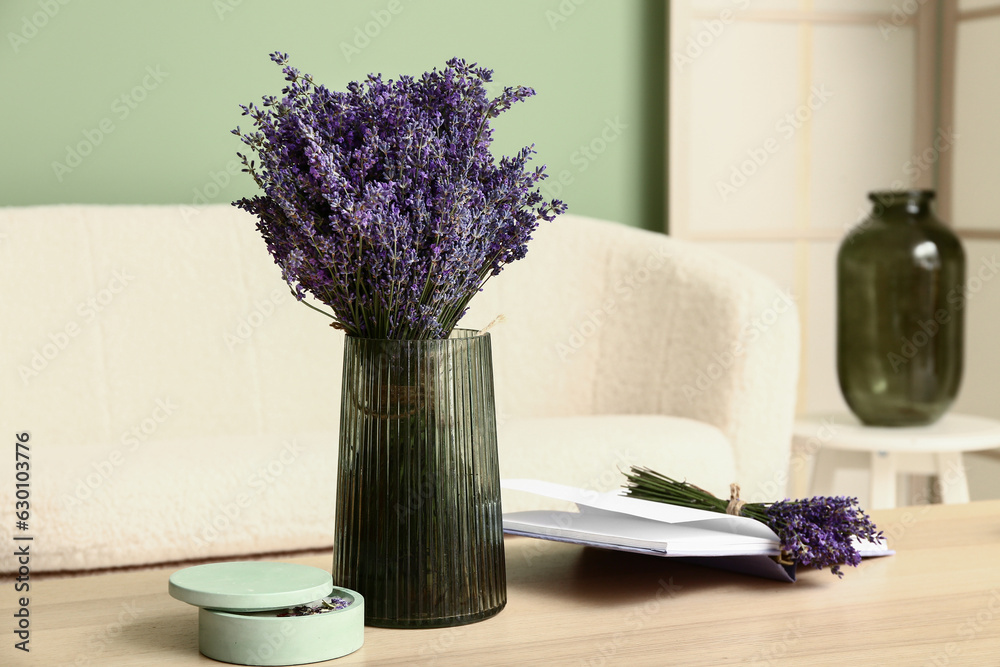 Vase with beautiful lavender flowers, candle and book on table in interior of living room, closeup