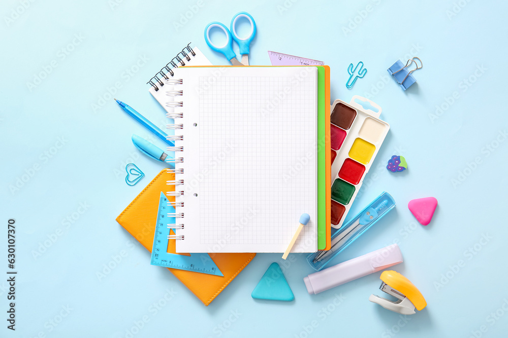 Composition with blank notebook and different school stationery on blue background