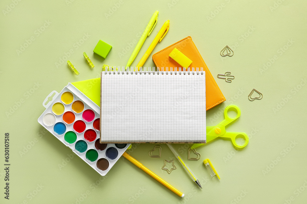 Composition with blank notebook and different school stationery on green background