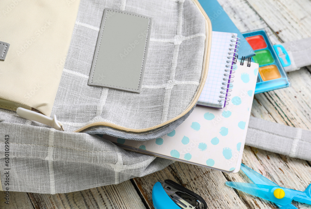 Grey school backpack with notebooks and watercolors on white wooden background