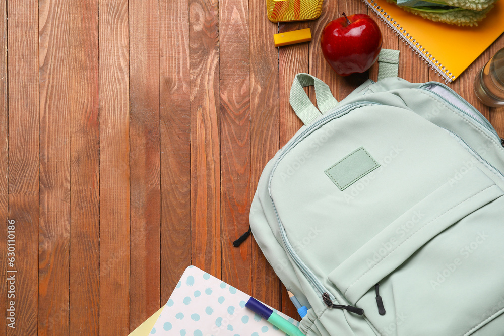 Green school backpack with apple and different stationery on wooden background