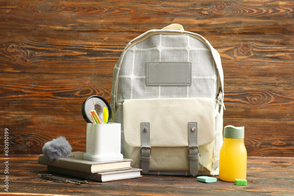 Grey school backpack with bottle of juice, books and stationery on wooden background