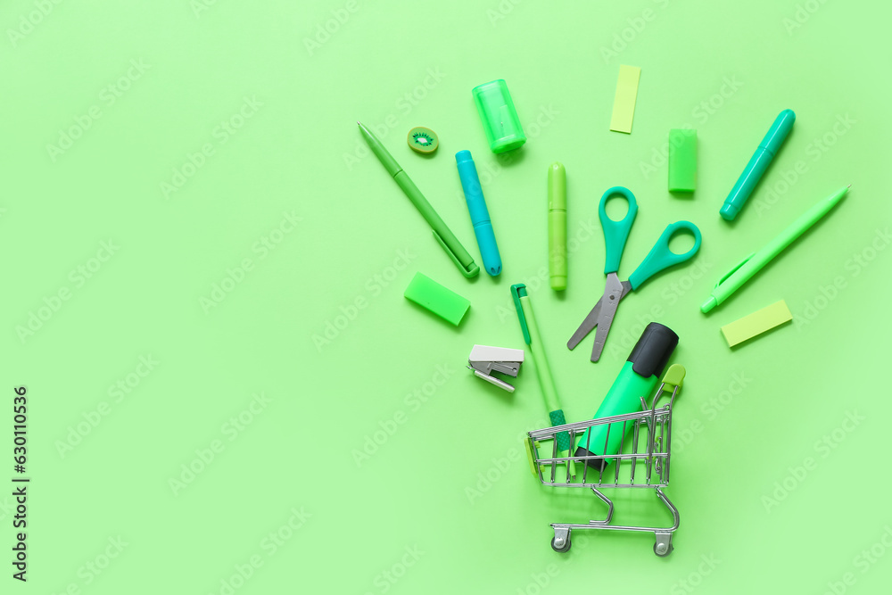 Shopping cart with different stationery on green background