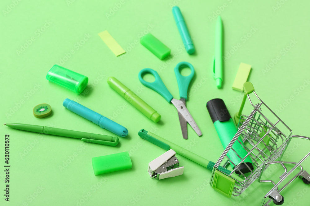 Shopping cart with different stationery on green background