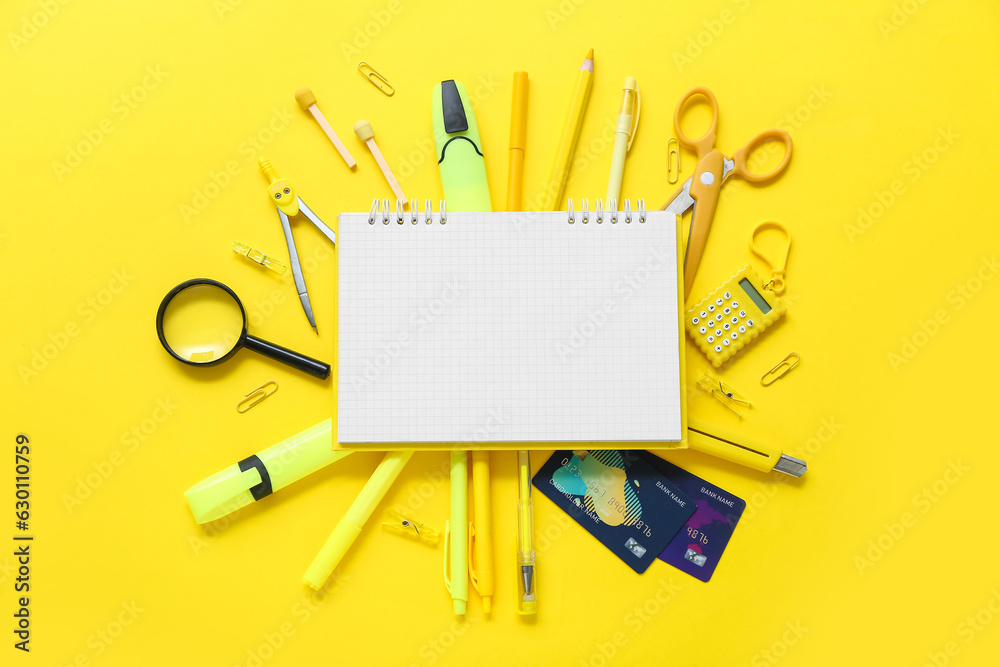 Blank notebook with credit cards and different stationery on yellow background