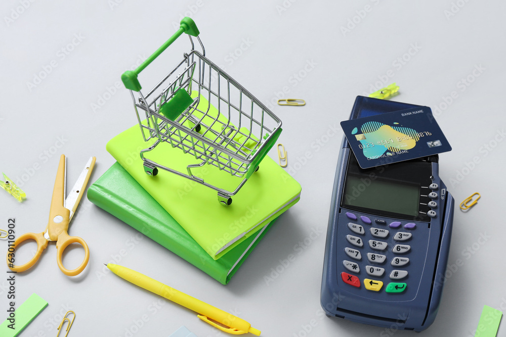 Payment terminal, credit card and shopping cart with different stationery on grey background