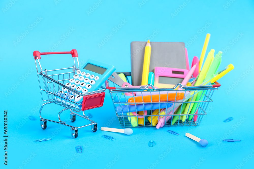 Shopping cart and basket with different stationery on blue background