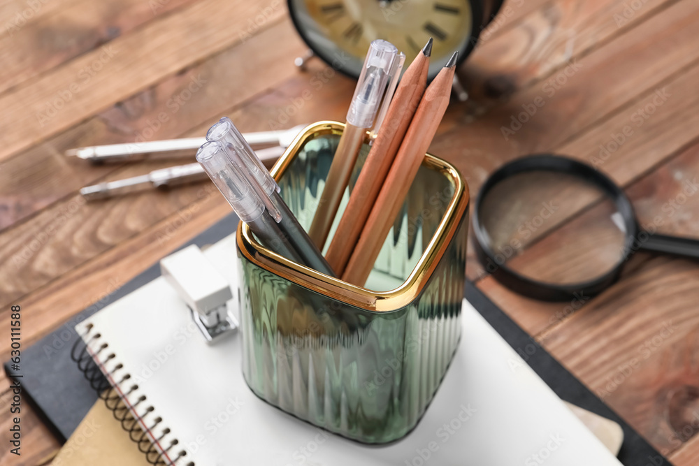 Glass holder with pens, pencils and notebooks on wooden table