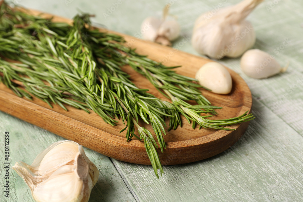 Board with fresh rosemary and garlic on color wooden background, closeup