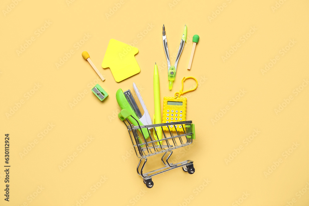 Shopping cart with various stationery on color background