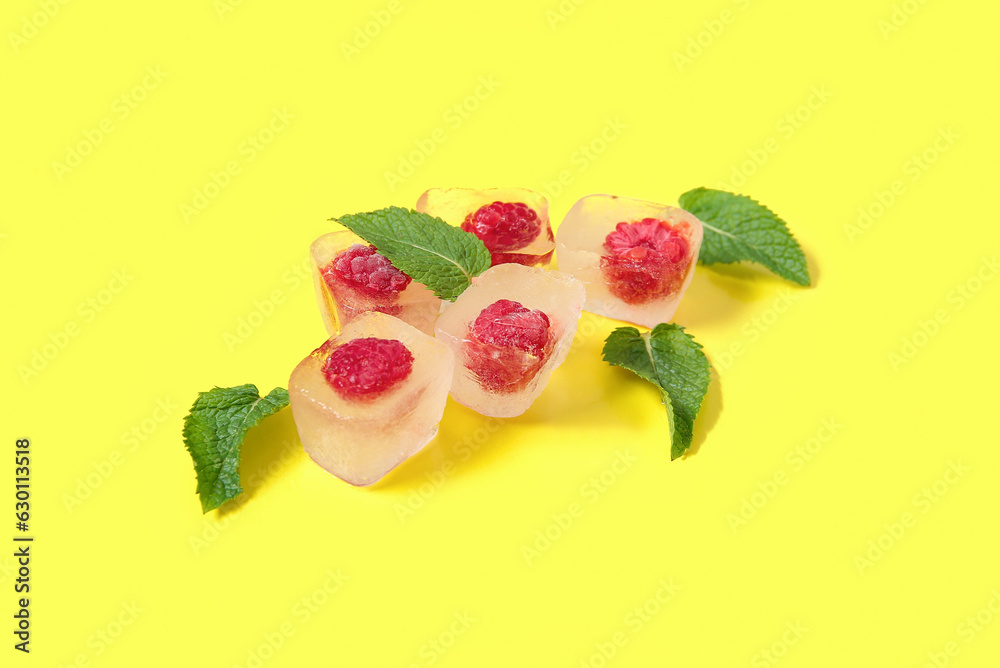 Frozen raspberries in ice cubes and mint on yellow background