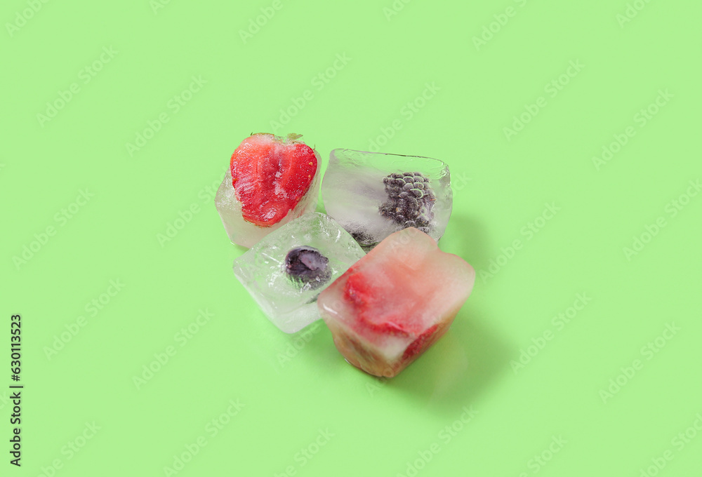 Frozen berries in ice cubes on green background