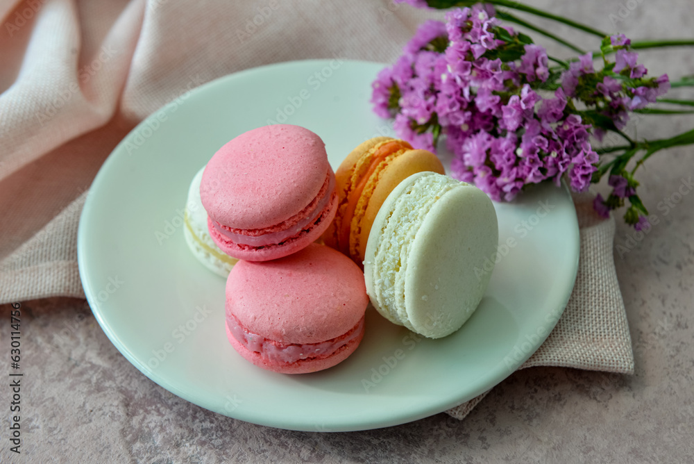 Plate with sweet macaroons and beautiful flowers on pink background