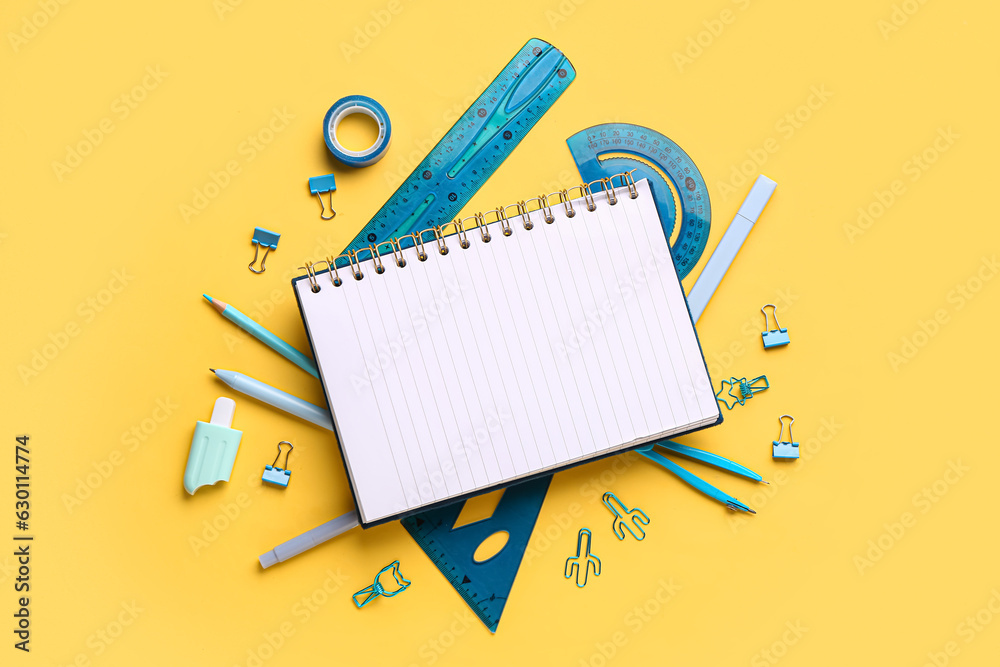 Notebook with different stationery supplies on yellow background