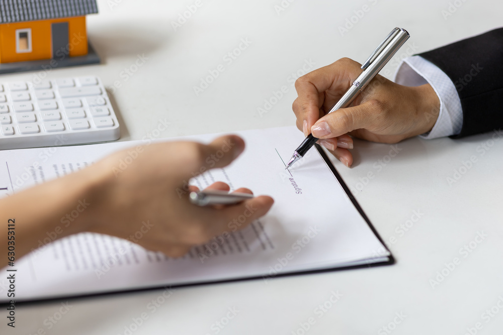 Real estate agent holding pen pointing at contract document for client to sign home purchase agreeme