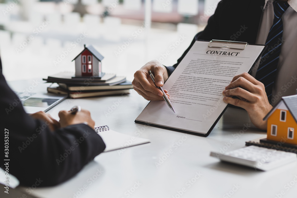 Real estate agent holding pen pointing at contract document for client to sign home purchase agreeme