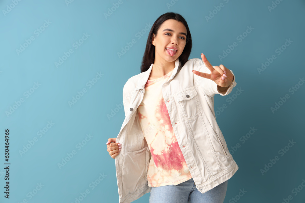 Young woman in tie-dye t-shirt showing victory gesture on blue background