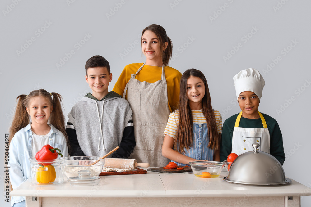 Female chef with group of little children during cooking class on light background