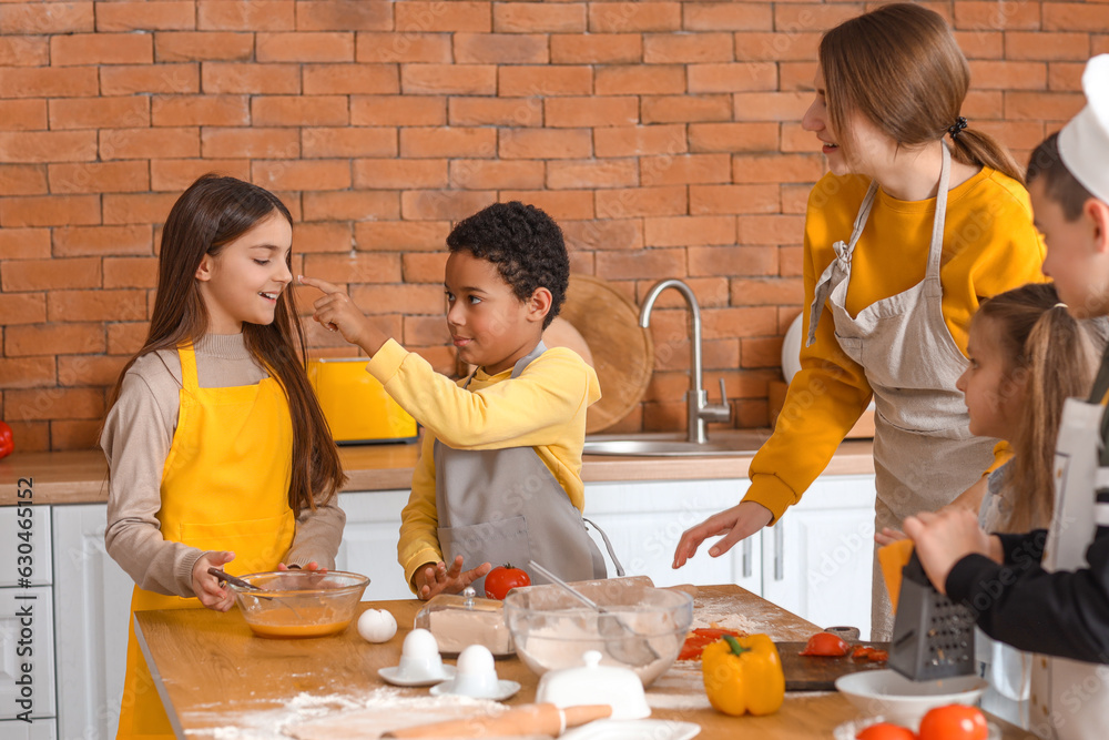 Female chef with group of little children preparing pizza during cooking class in kitchen