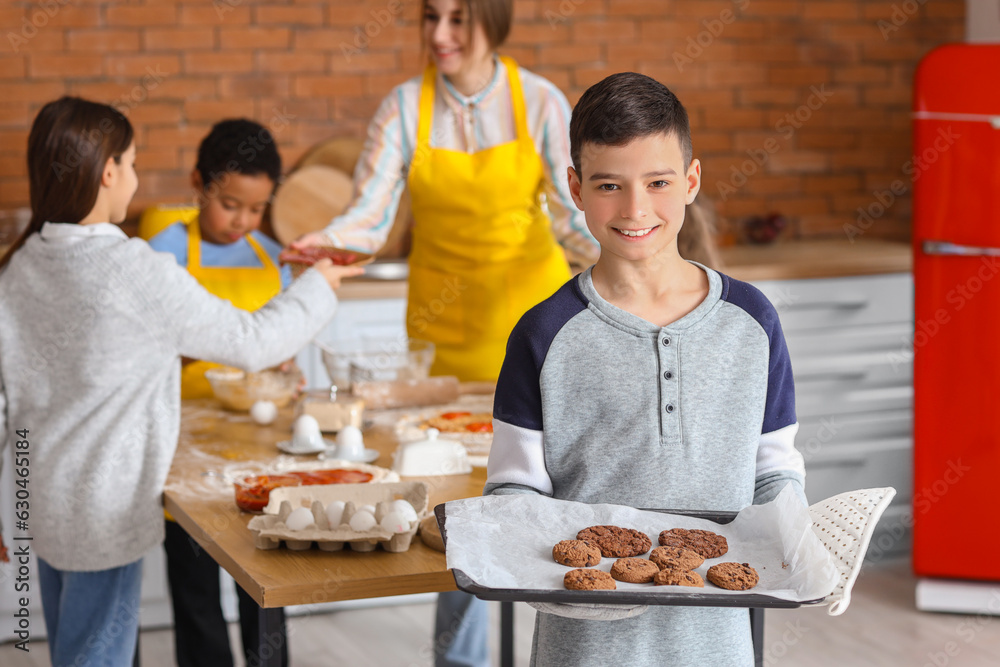 Little boy with prepared cookies during cooking class in kitchen