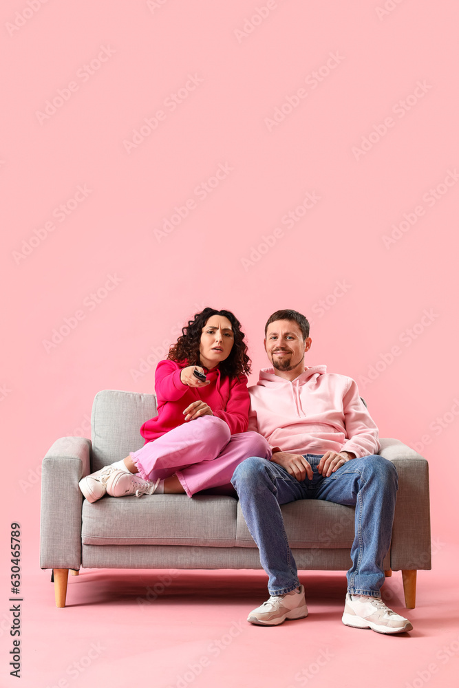 Young couple watching TV on pink background