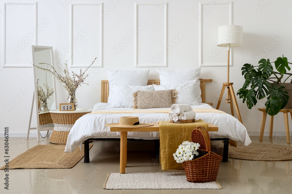 Interior of light bedroom with chrysanthemum flowers in basket and blooming tree branches on bedside