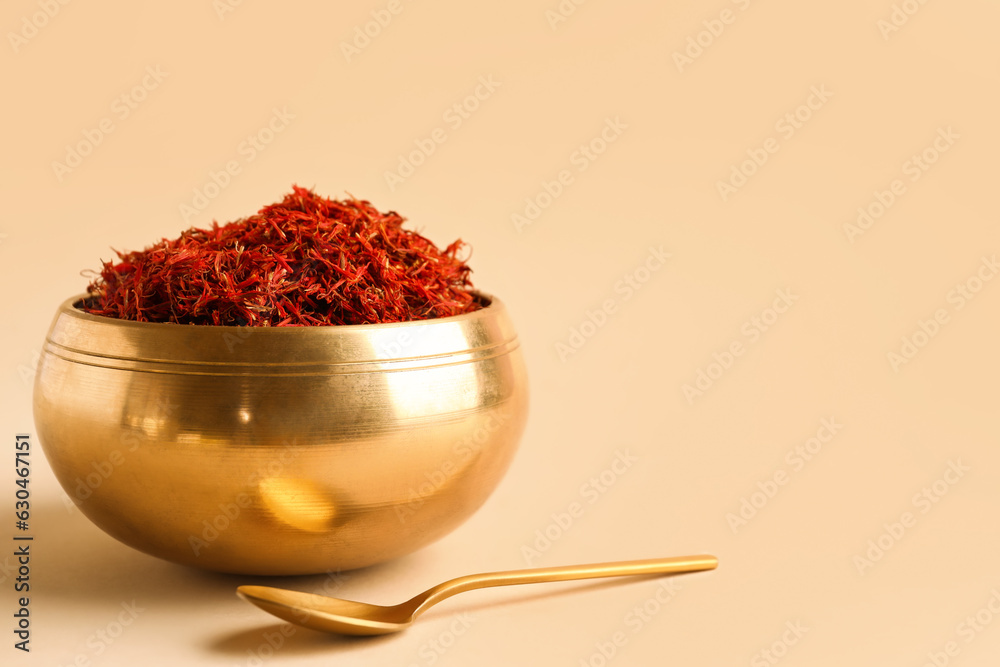 Golden bowl and spoon with pile of saffron on light background