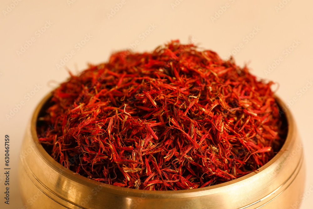 Golden bowl and spoon with pile of saffron on light background