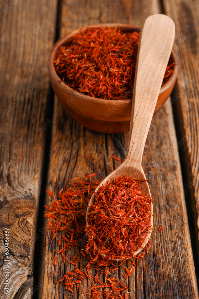 Bowl and spoon with pile of saffron on wooden background