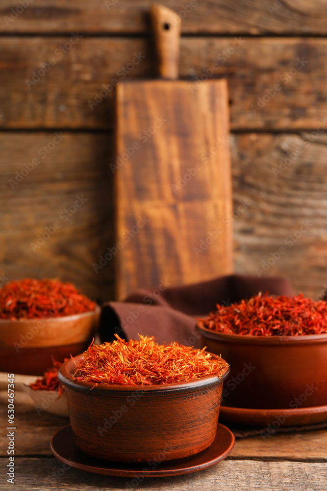 Bowls with pile of saffron on wooden background