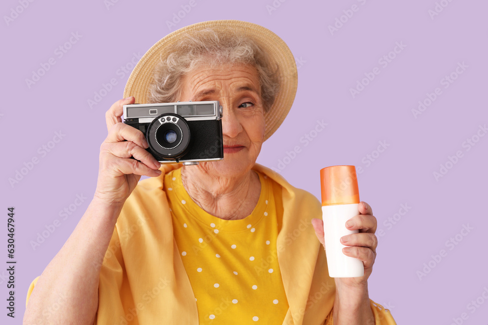 Senior woman with sunscreen cream and photo camera on lilac background, closeup