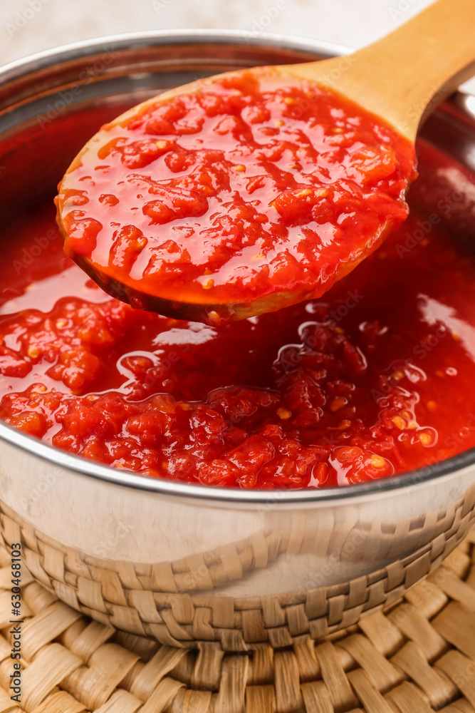 Saucepan and spoon with tasty tomato sauce on table, closeup