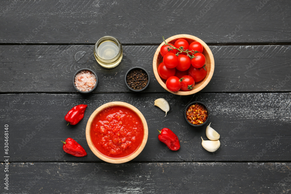 Bowls with tasty tomato sauce and ingredients on dark wooden background