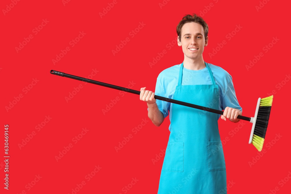 Male janitor with broom on red background