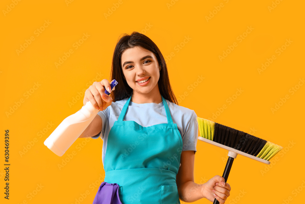 Female janitor with broom and detergent on yellow background