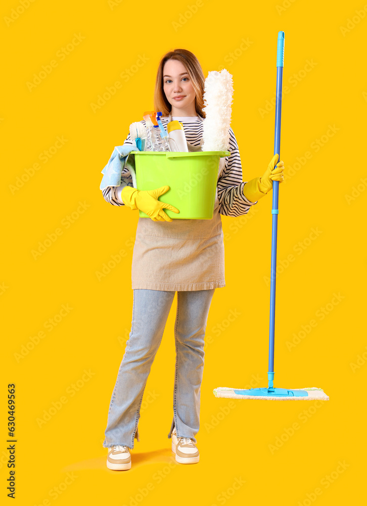 Young woman with cleaning supplies on yellow background