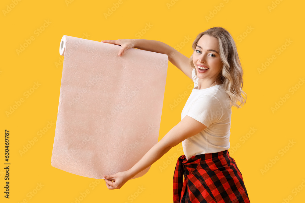 Young woman with wallpaper roll on yellow background