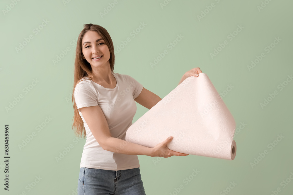 Young woman with wallpaper roll on green background