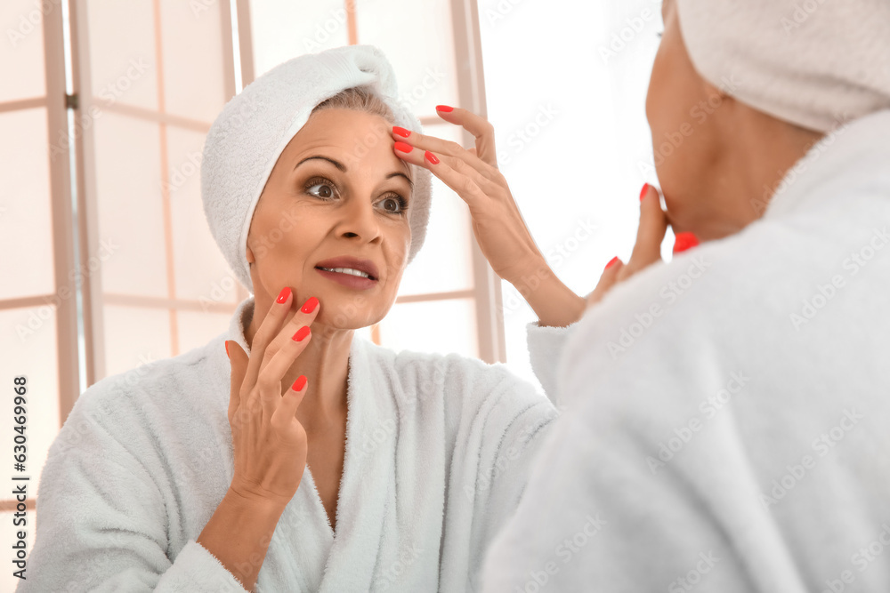 Mature woman applying facial cream near mirror in bathroom, closeup