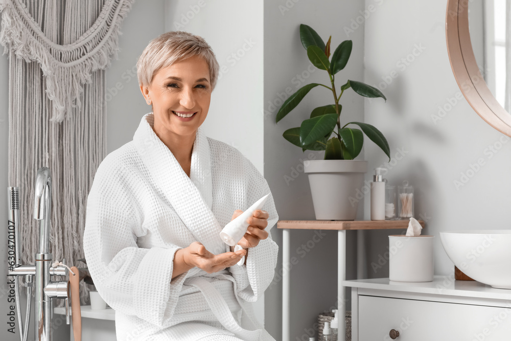 Mature woman applying hand cream in bathroom