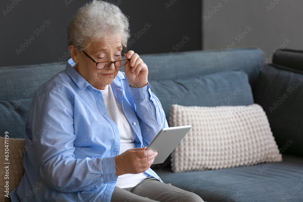 Senior woman in eyeglasses using tablet computer at home