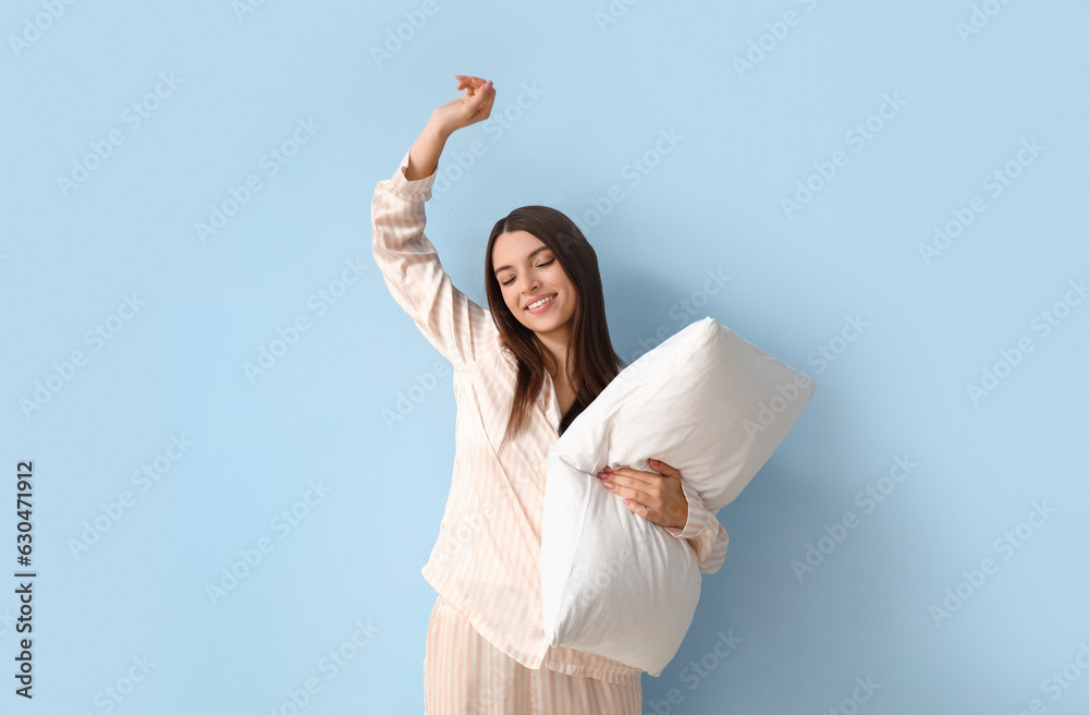 Young woman in pajamas with pillow on blue background